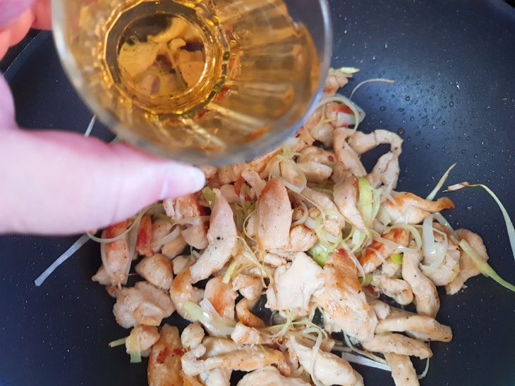 Uma frigideira com o frango, o alho-poró e o vinho.