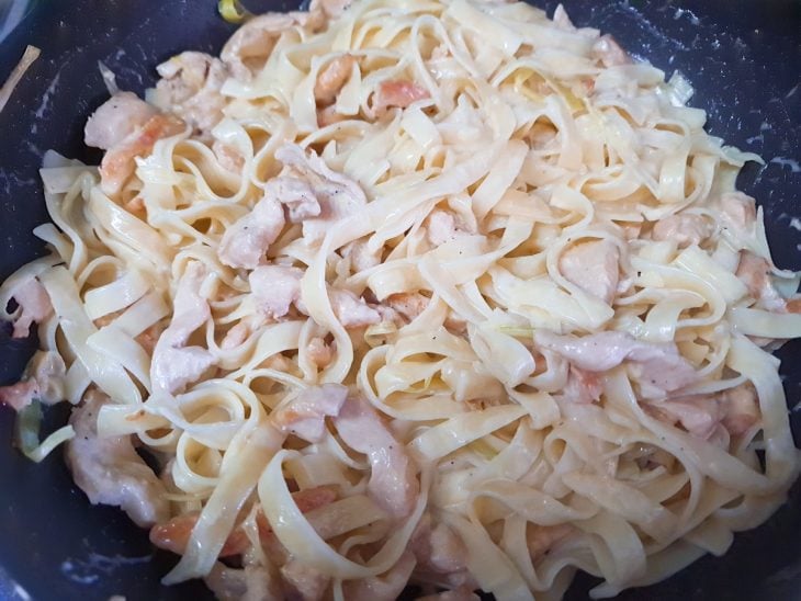 Uma frigideira com o macarrão, frango e molho misturados.