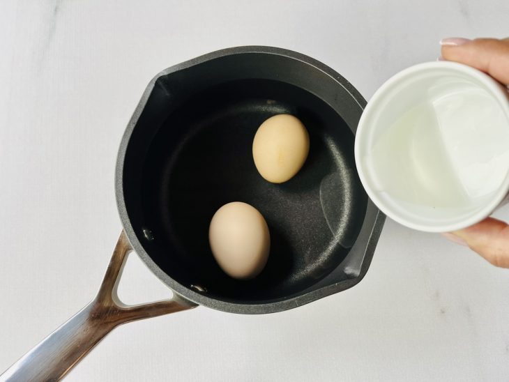 Ovos cozinhando em água com vinagre em panela média.