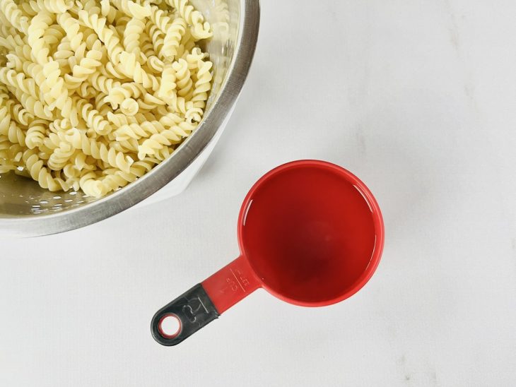 Macarrão escorrido, com uma xícara da água do cozimento separada.