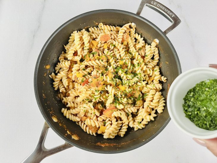 Macarrão sendo misturado ao molho encorpado com cheiro-verde.