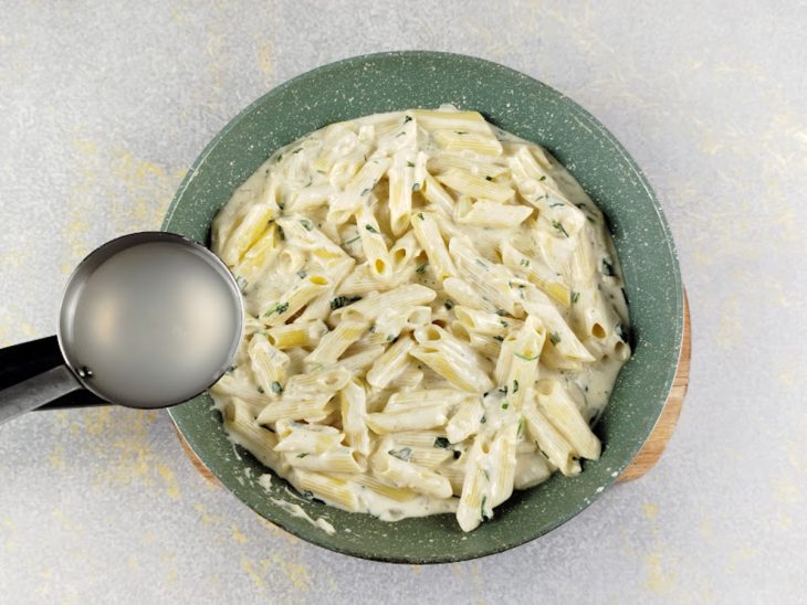 Na panela, uma concha da água do cozimento do macarrão sendo adicionada.