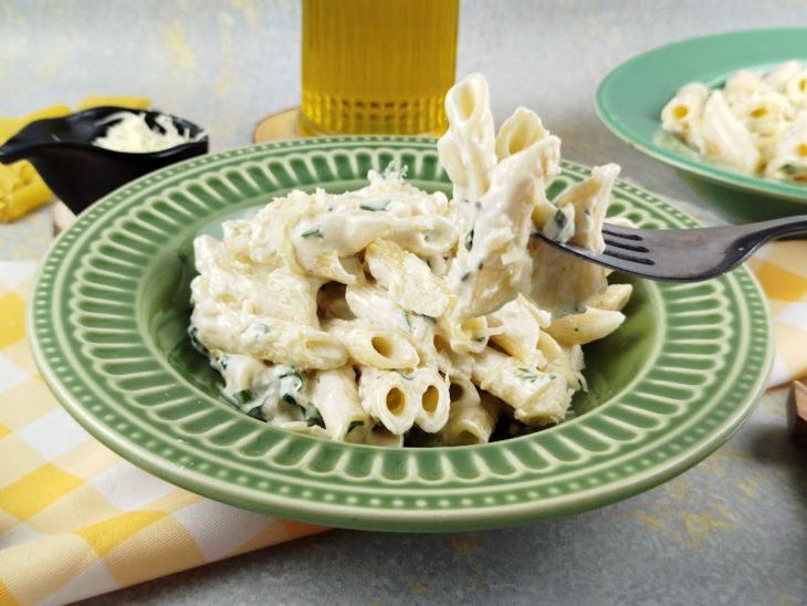 Macarrão pronto e servido em prato, garfo tirando uma porção.