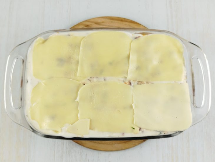 Refratário com camada de molho branco e queijo mussarela.