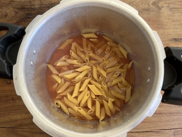 Panela com macarrão cru, água e molho de tomate.