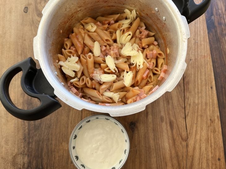 Macarrão cozido com pedaços de mussarela e um potinho de creme de leite ao lado.