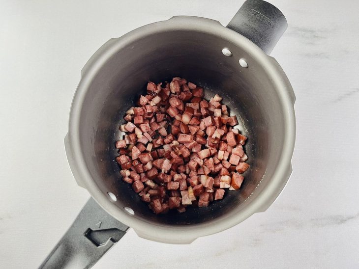 Cubos de calabresa e bacon na panela de pressão regada com um fio de azeite.