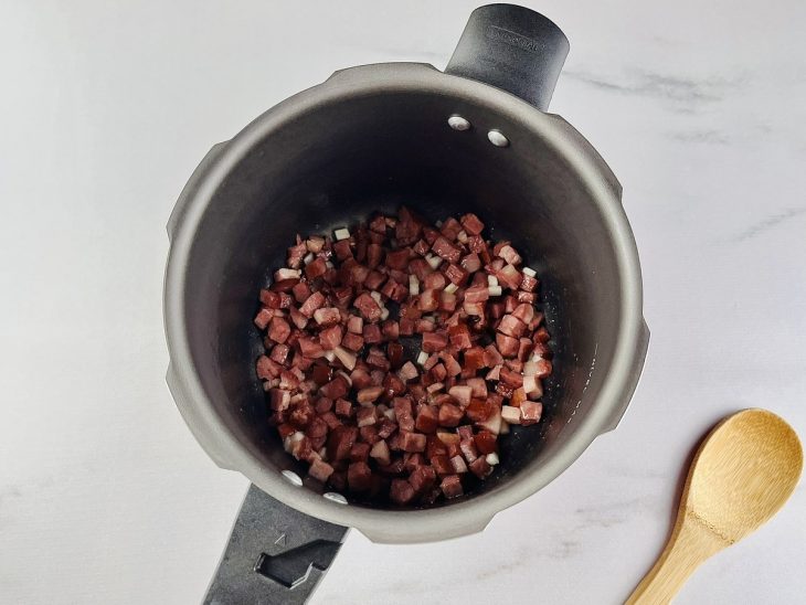 Cebola e alho adicionados na panela de pressão com cubos de bacon e calabresa.