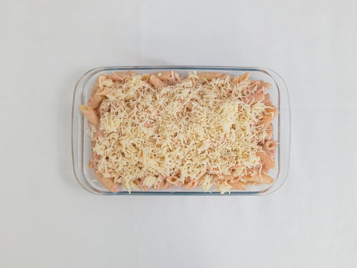 Macarrão colocado em um refratário de vidro com queijo parmesão ralado salpicado na superfície.