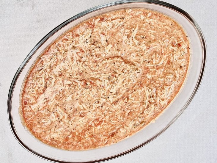 Refratário de vidro com molho de tomate, mussarela ralada, requeijão, parmesão ralado, óleo, pimenta, sal e orégano misturados.
