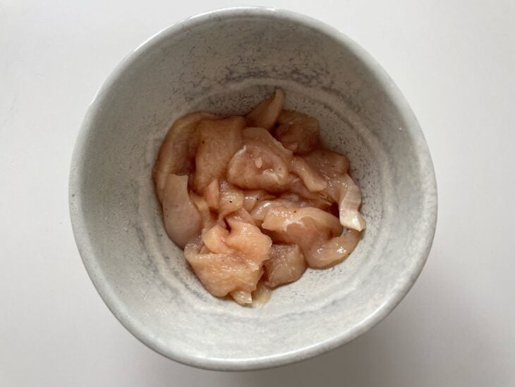 Peito de frango sendo temperado com sal e pimenta-do-reino em uma tigela.