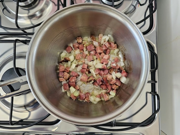 Uma panela fritando bacon em cubos, alho e cebola.