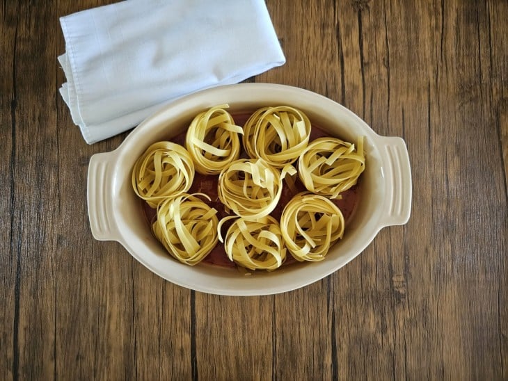 Uma travessa forrada com molho e com macarrões do tipo ninho.