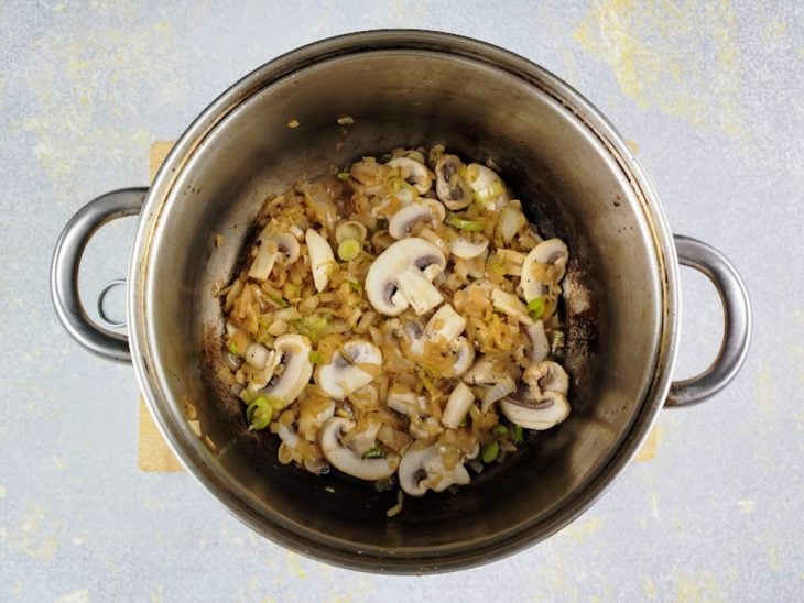 Uma panela com cebola, cogumelos e alho-poró refogados.
