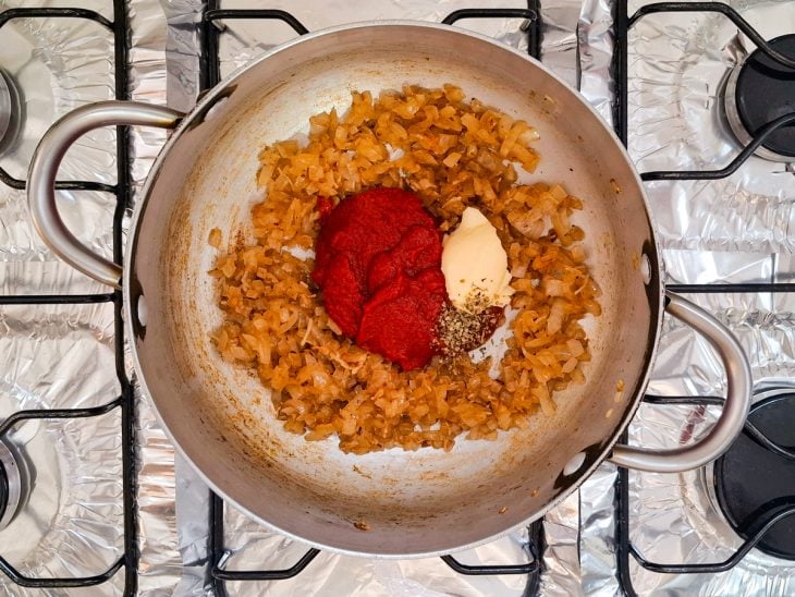 Extrato de tomate, manteiga, orégano e pimenta-do-reino adicionados a panela com alho e cebola.