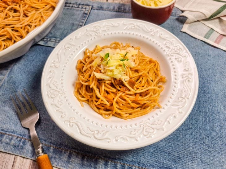 Prato com uma porção da macarronada finalizada com queijo parmesão ralado.