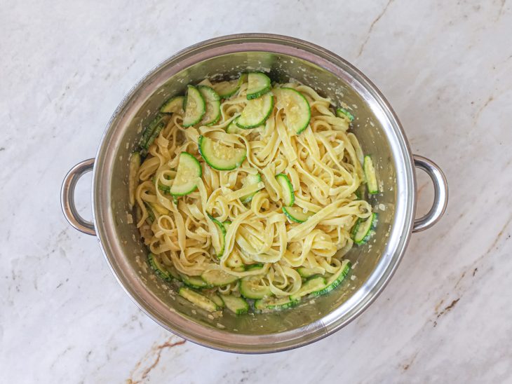 Macarrão, molho e uma concha de água adicionados a panela.