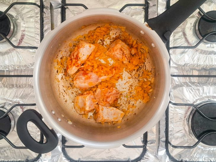 Cebola e frango temperado com sal e colorau refogando em uma panela de pressão com azeite.