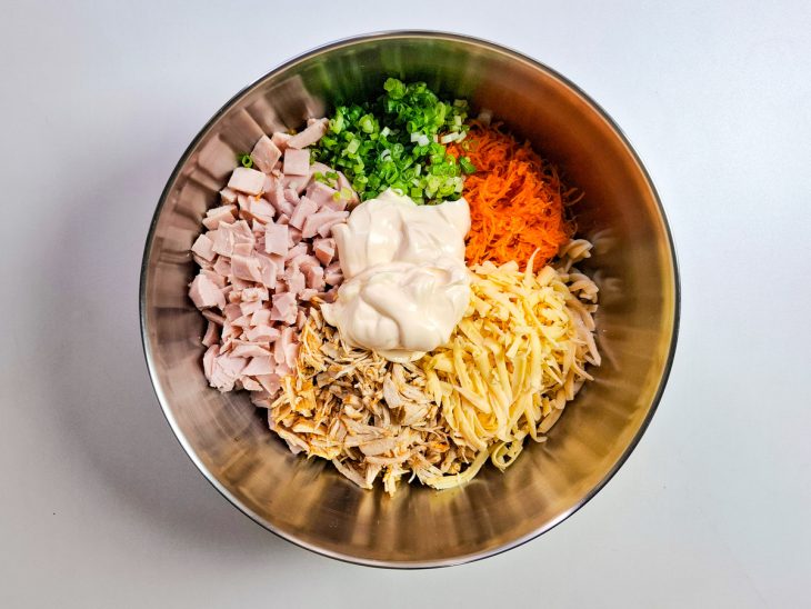 Cenoura, milho, peito de peru, mussarela, frango desfiado, cebolinha, cebola e maionese adicionados a tigela com macarrão.
