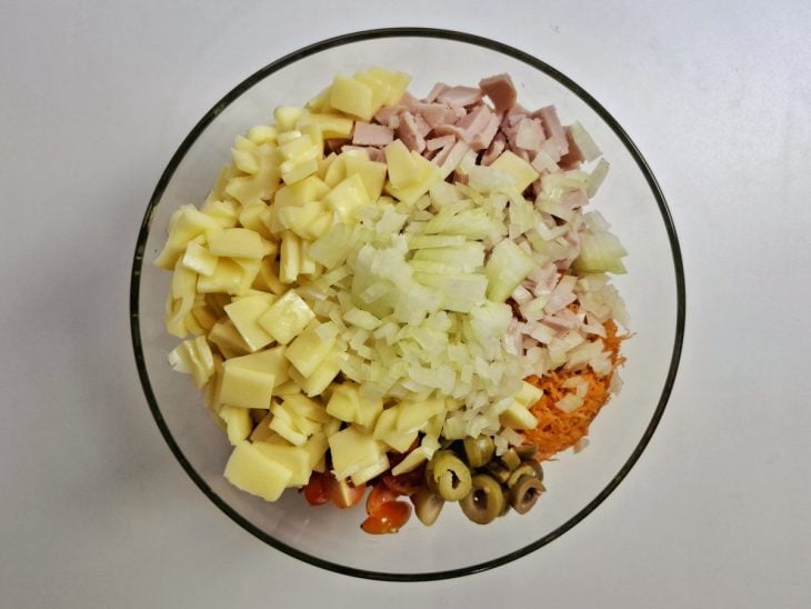 Cenoura ralada, presunto, azeitonas, tomate, cebola, queijo e uvas-passas adicionados a travessa de vidro.