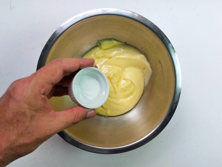Um recipiente contendo maionese sendo temperada com sal.