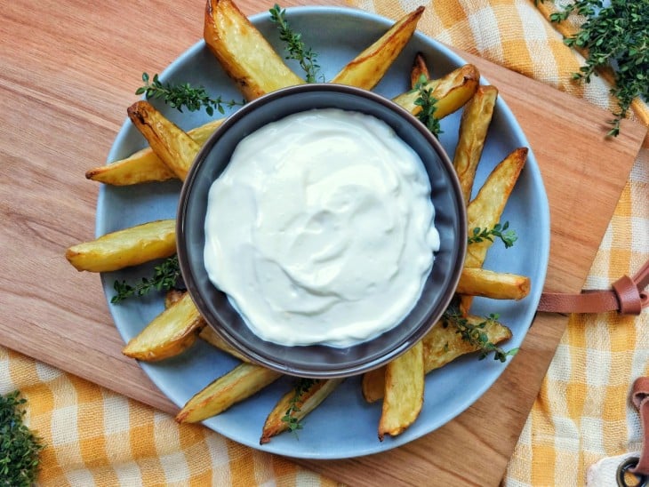 Maionese caseira sem ovos pronta, disposta em uma cumbuca e servida com algumas batatas palitos.