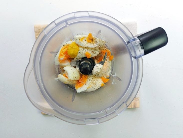 Um liquidificador com ovos cozidos, mostarda, sal, pimenta e iogurte.