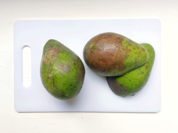 Um abacate inteiro e outro cortado ao meio.