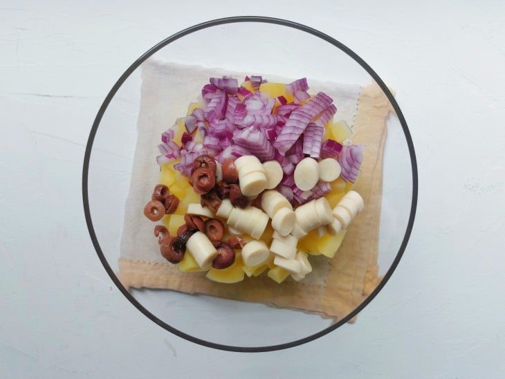 Um recipiente contendo batatas, azeitonas, palmito e cebola.
