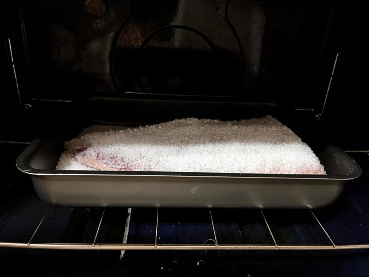 Uma forma com uma peça de maminha coberta de sal grosso no forno.