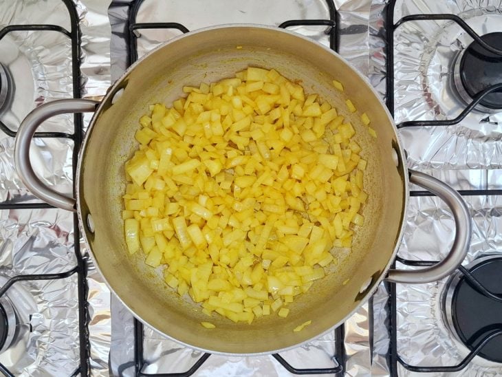 Uma panela com óleo, cebola e açafrão.
