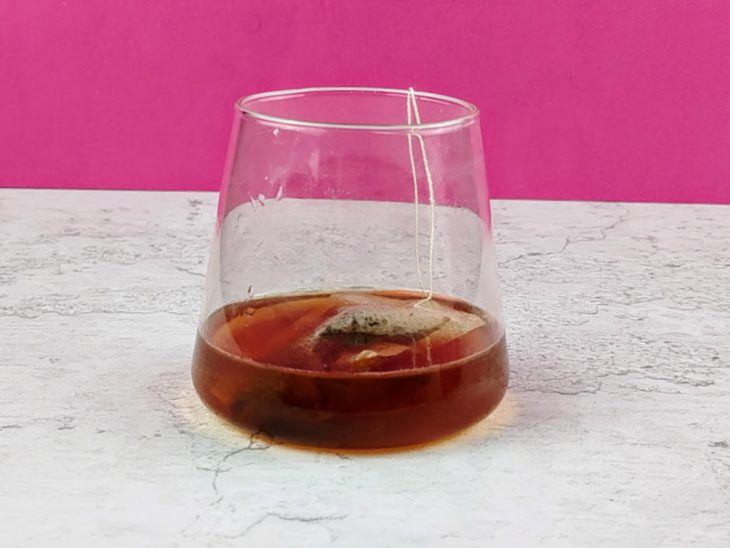 Sachê de chá infusionado em copo com água.