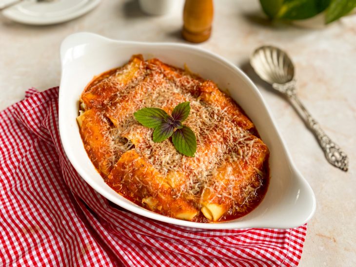 Canelones assados e finalizados com folhas de manjericão, prontos para consumo.