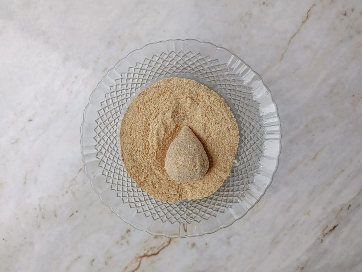 Coxinha empanada num recipiente com farinha de rosca.