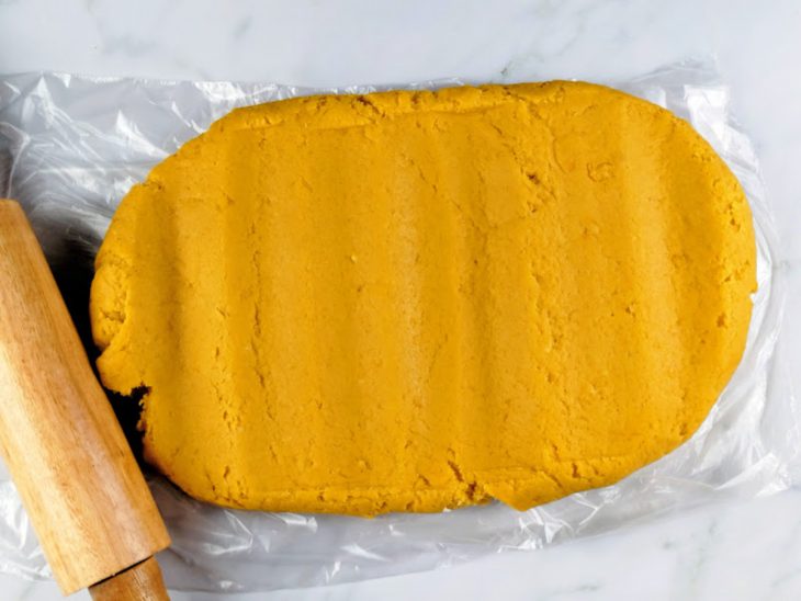 Massa de coxinha aberta com um rolo sobre um pedaço de plástico.