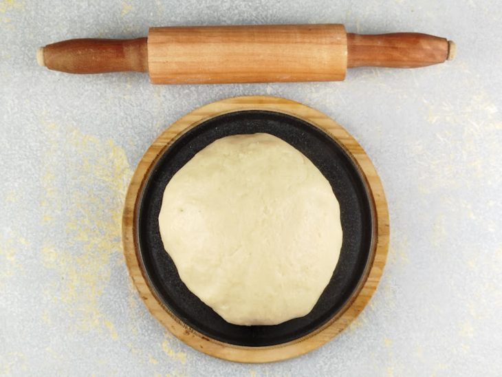 Massa numa bancada com rolo de macarrão próximo.