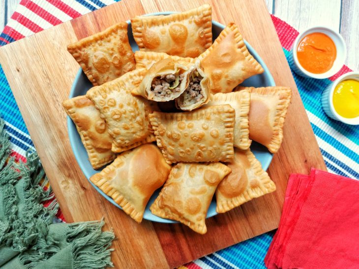 Pastéis fritos e um deles cortado ao meio mostrando o recheio de carne moída.