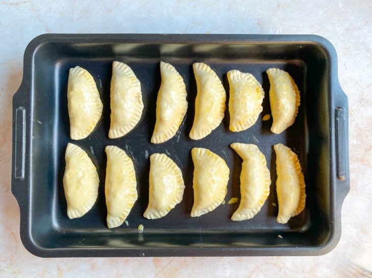 Pastéis fechados e com gema pincelada na superfície, acomodados na assadeira untada.