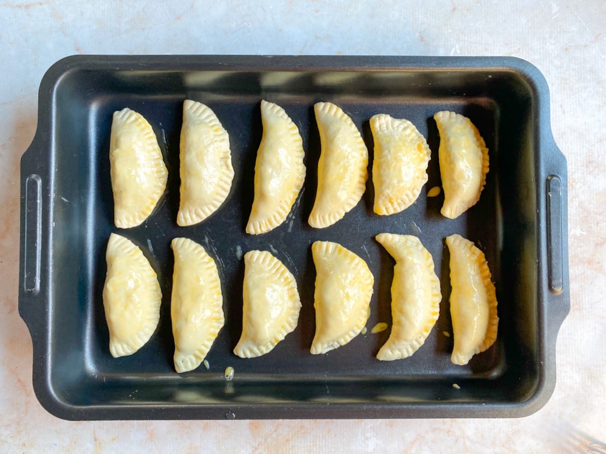 Pastéis fechados e com gema pincelada na superfície, acomodados na assadeira untada.