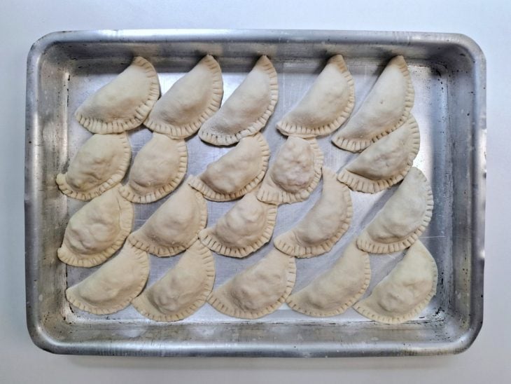 Pastéis recheados e acomodados em uma assadeira.