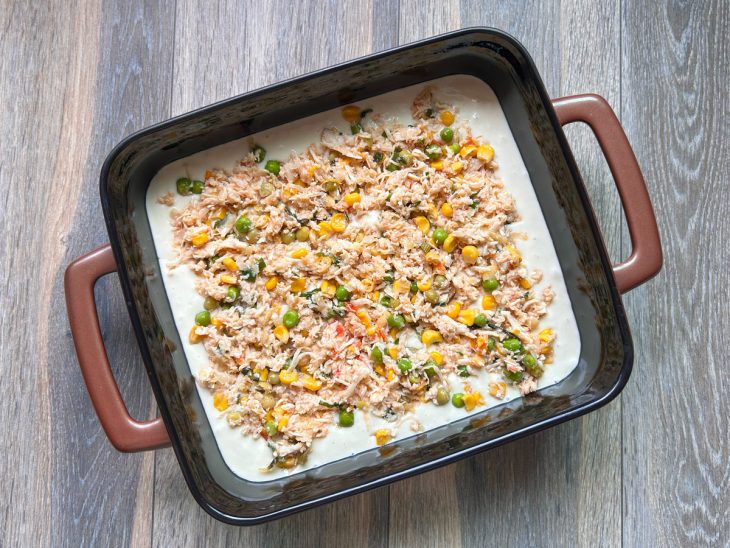Forma com uma porção de massa e uma camada de recheio de frango desfiado.