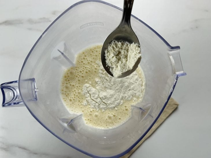 Um liquidificador com a mistura de leite, ovos, óleo, sal, amido de milho e farinha.