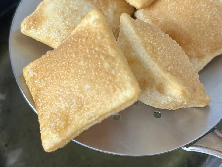 Massinha frita sendo retirada da panela com óleo quente.