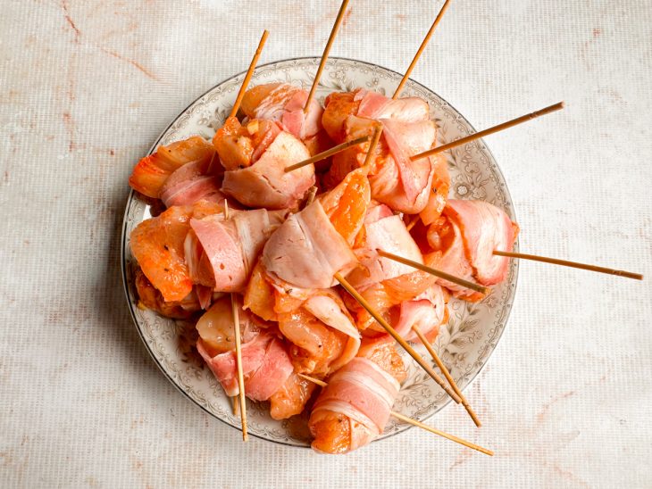 Pedaços de frango sendo enrolados com tiras de bacon.