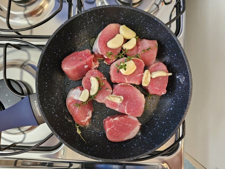 Mignon suíno ainda cru em uma frigideira com alguns temperos.