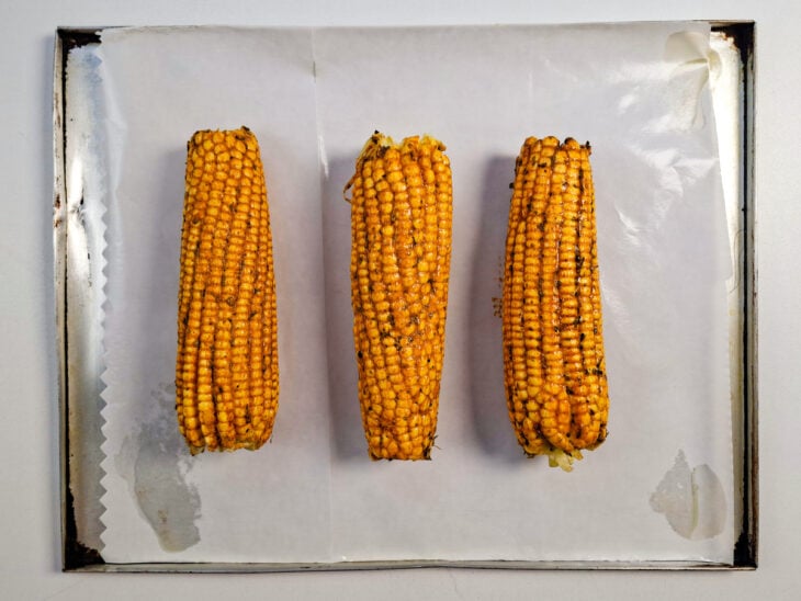 Milhos temperados acomodados em uma assadeira antes de serem levados ao forno.