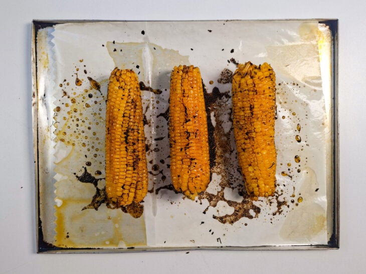 Espigas assando no forno e sendo viradas durante o preparo para dourar por igual.