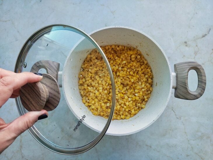 Milho cozinhando em panela tampada até ficar macio.