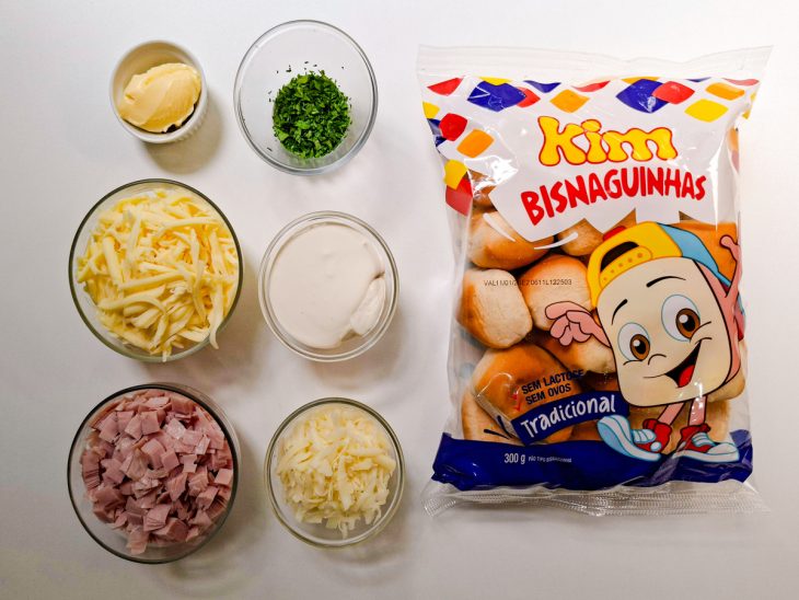 Ingredientes separados na bancada, com queijo, presunto e bisnaguinhas visíveis.