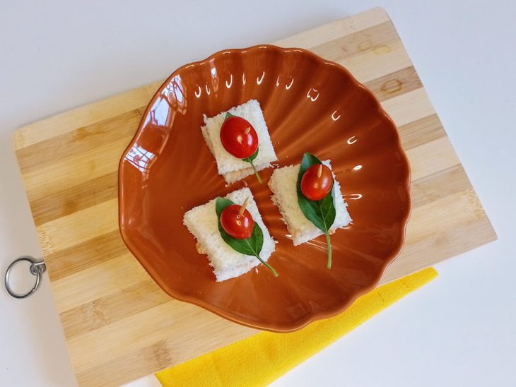 Um prato com minissanduíches decorados com tomates e folhas de manjericão.